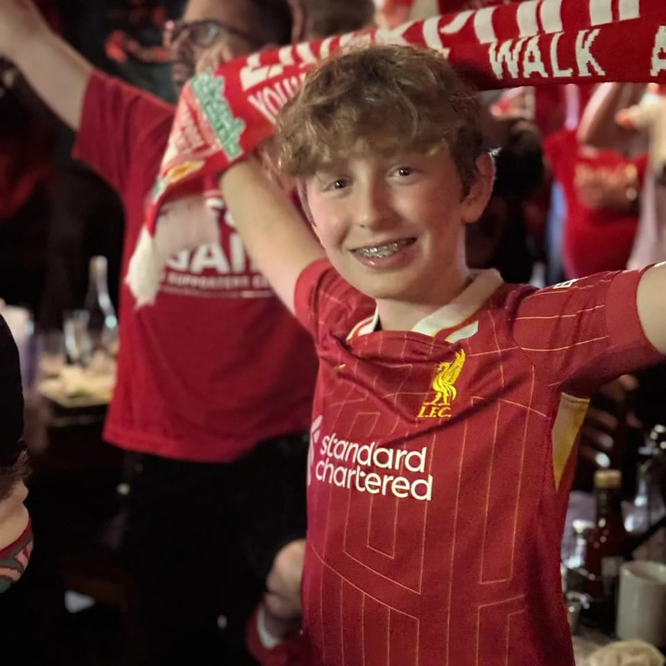 A young Liverpool supporter holding a scarf during a match-day celebration.