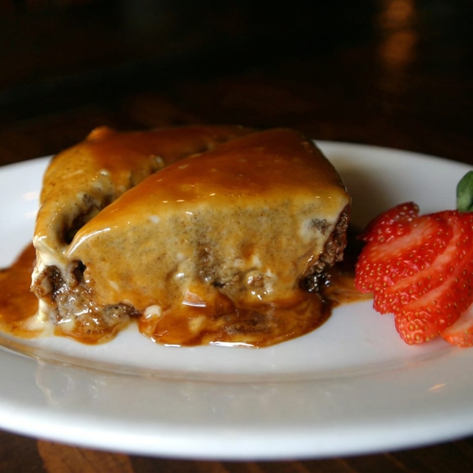 Cheesy baked entrée topped with melted cheese and gravy, served with sliced strawberries on a white plate.