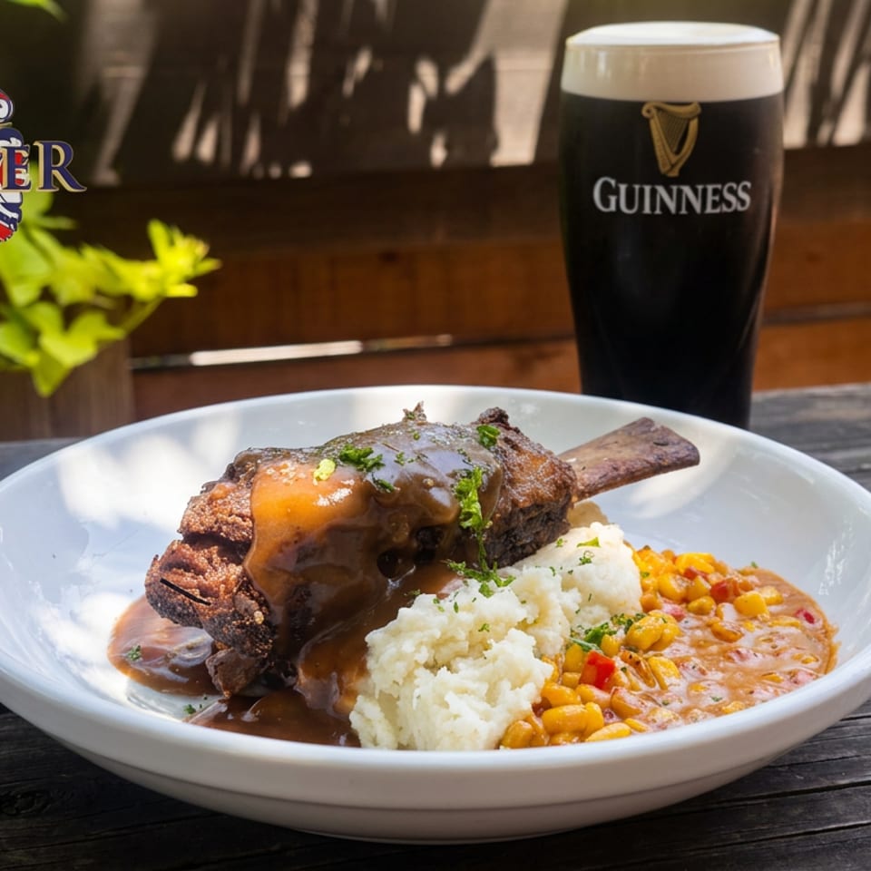 Braised meat with mashed potatoes and vegetables served alongside a pint of Guinness on a sunny outdoor table.