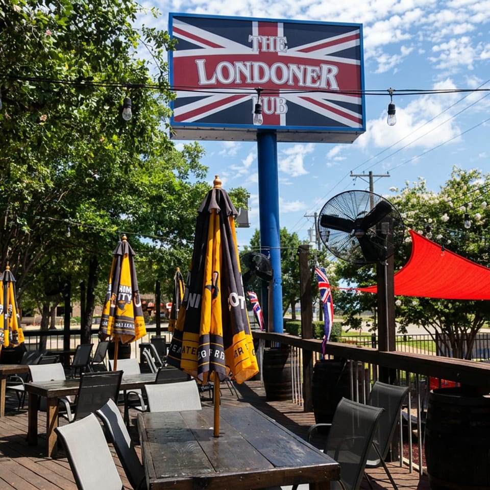 The Londoner pub’s outdoor patio features Union Jack signage, tables, umbrellas, string lights, fans, and colorful shade sails.