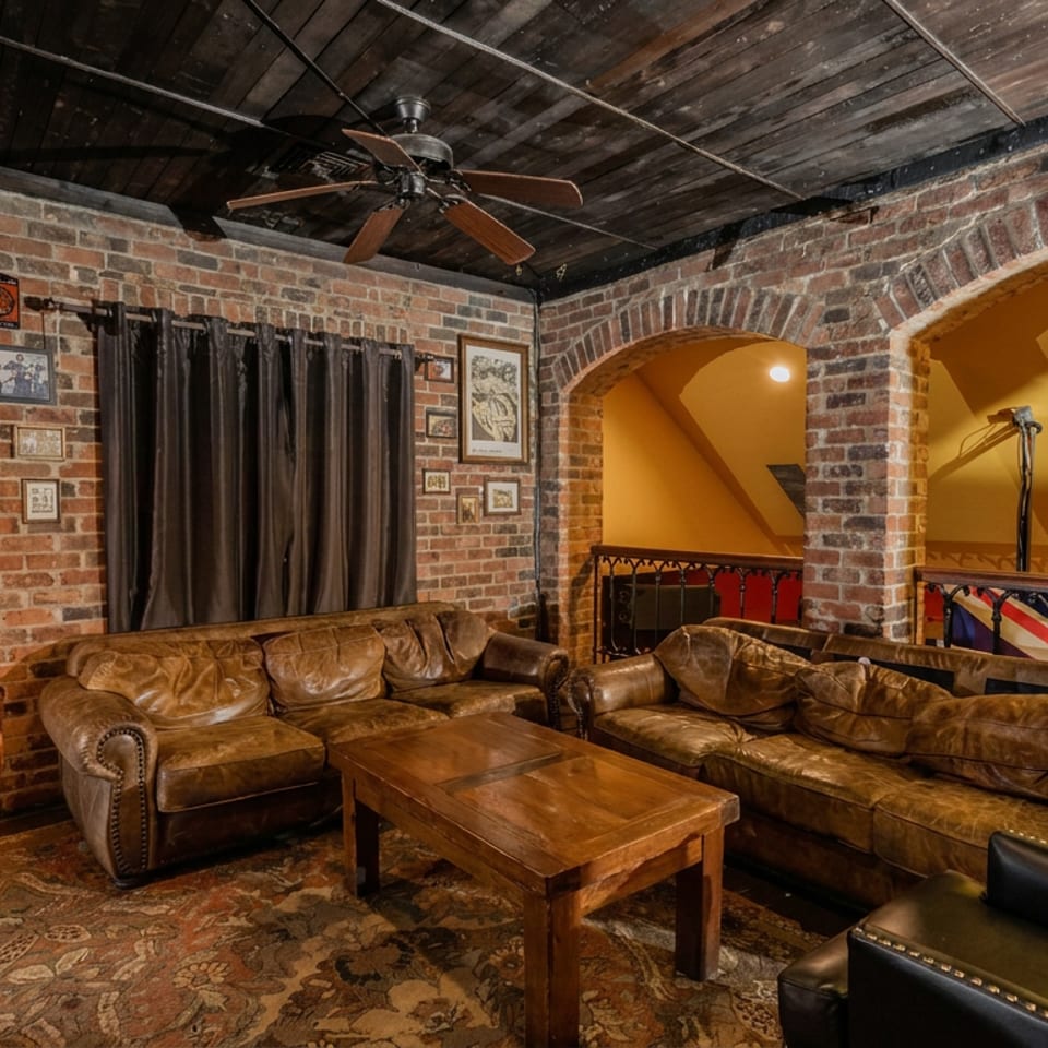 Cozy restaurant lounge with leather sofas, wooden coffee table, exposed brick arches, framed artwork, and warm ambient lighting.